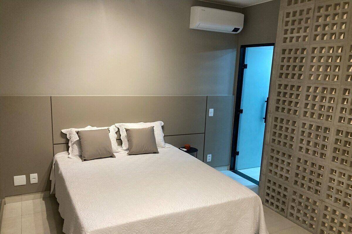 A bedroom with a bed, a nightstand, a wall-mounted air conditioner, and a door leading to a balcony.