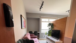 Moderni olohuone, jossa on musta nojatuoli, vaaleanpunainen sohva ja televisio valkoisessa kaapissa.