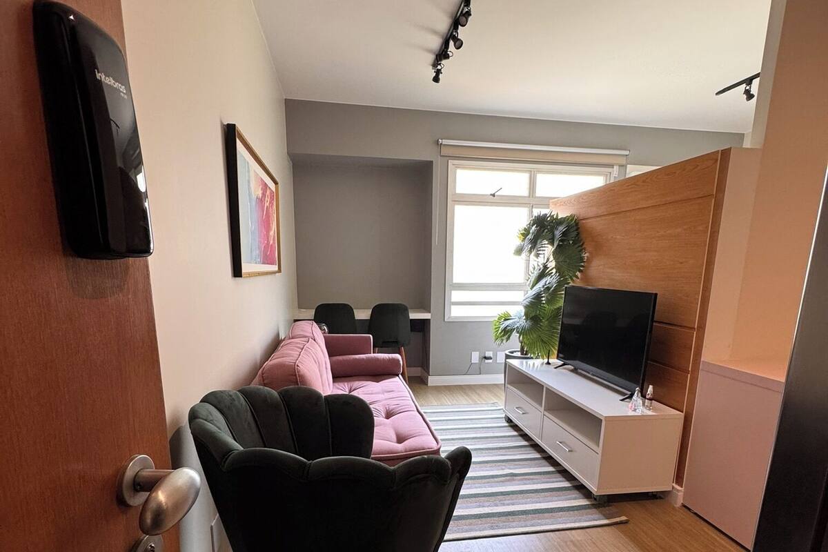 A modern living room with a black armchair, pink sofa, and a TV on a white cabinet.