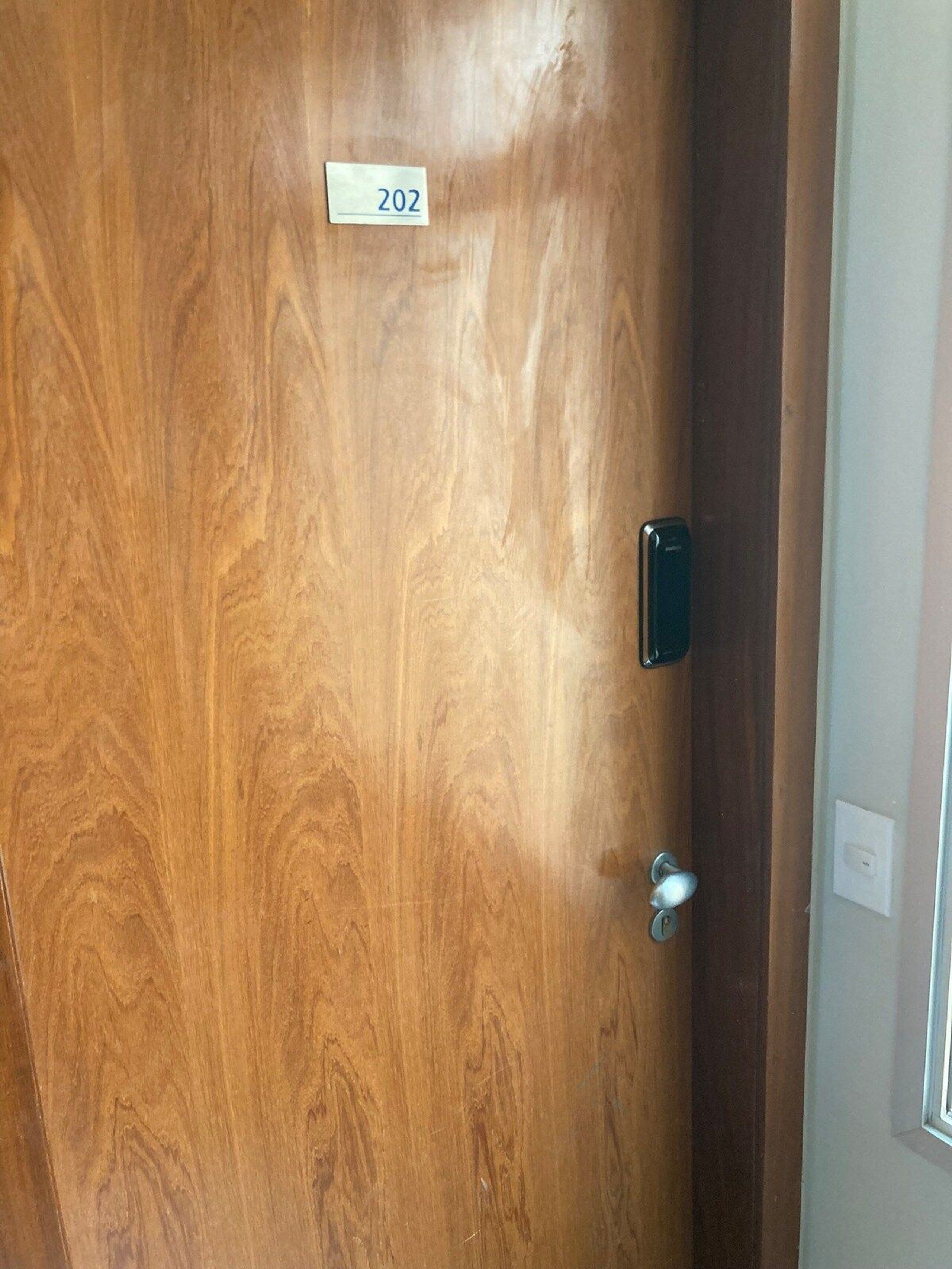 A wooden door with a number plate labeled "202" and a modern door handle.