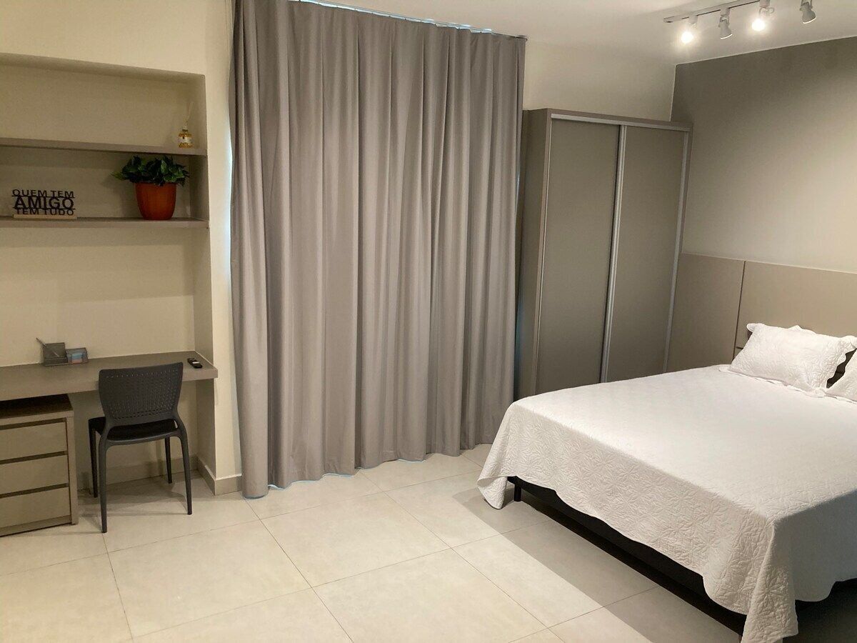 Una habitación de hotel moderna con cama, escritorio, silla y un ventanal con cortinas.