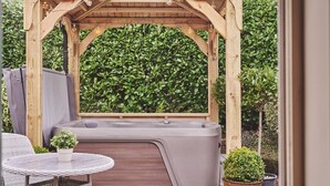 A wooden gazebo with a hot tub underneath, surrounded by lush greenery. - Hollington Barns - Luxury Cottages (Ashbourne)