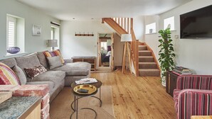 A cozy living room with a sofa, a coffee table, and a staircase leading to another room. - Hollington Barns - Luxury Cottages (Ashbourne)
