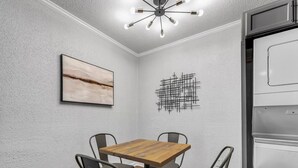 Zona pranzo con tavolo in legno e quattro sedie, una lampada a sospensione, un'opera d'arte astratta appesa al muro e un frigorifero.