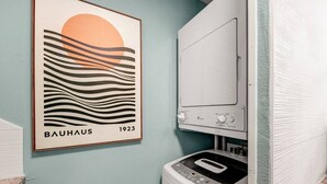 A laundry room with a wall-mounted washing machine, a framed Bauhaus poster from 1923, and a light blue wall. - Bauhaus-1st Floor, King Beds, Walk to A&M Campus (Bryan)