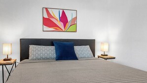 A neatly made bed with a patterned bedspread, two bedside lamps, and a colorful abstract painting above the bed. - BethyKay: 2 Bedroom, Walk to A&M, Comfy King Beds (Bryan)