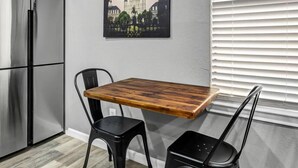 A modern kitchen with a stainless steel refrigerator, a wooden dining table, two black chairs, and a cityscape painting on the wall. - Big Easy: 2 Bedrooms, 2nd floor, Walk to A&M, Comfy King Beds (Bryan)