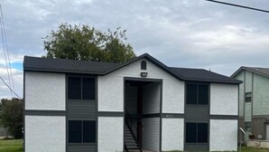 A two-story building with a garage entrance, a visible address number, and a small front yard. - Big Easy: 2 Bedrooms, 2nd floor, Walk to A&M, Comfy King Beds (Bryan)
