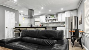 A modern kitchen with white cabinets, stainless steel appliances, and a black leather sofa in the living area. - Big Easy: 2 Bedrooms, 2nd floor, Walk to A&M, Comfy King Beds (Bryan)