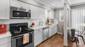 A modern kitchen with white cabinets, stainless steel appliances, and a wooden floor. - Blossom: Ground Floor, Comfy King Bed (Bryan)