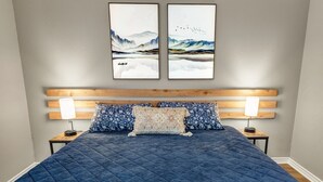 A bedroom with a large bed, two nightstands, a wooden headboard, and two framed artworks above the bed. - Blossom: Ground Floor, Comfy King Bed (Bryan)