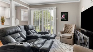 A living room with a black leather sofa, a beige armchair, and a flat-screen TV. - Blossom: Ground Floor, Comfy King Bed (Bryan)
