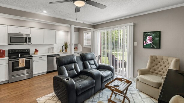A modern living room with a black leather sofa, a beige armchair, and a wooden coffee table. - Blossom: Ground Floor, Comfy King Bed (Bryan)