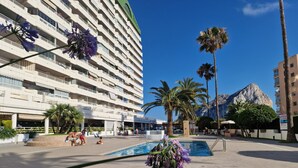 A hotel with a pool area, palm trees, and a mountain in the background.