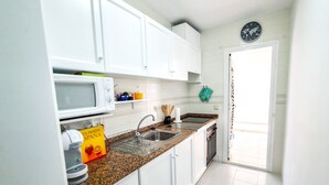 A modern kitchen with white cabinets, a granite countertop, a built-in microwave, and a stainless steel sink.