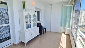 A spacious room with a large window, a white cabinet with glass doors, and a small table.
