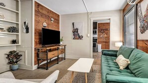 Uma sala de estar moderna com uma parede de destaque em madeira, uma televisão de tela plana, um sofá verde e uma mesa de centro branca.