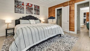 Um quarto com cama, mesas de cabeceira, um tapete estampado, uma parede de madeira e um guarda-roupa.