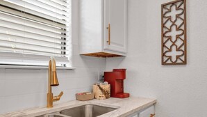 Una cocina con un lavamanos doble, un grifo dorado, una cafetera roja y un adorno de pared.