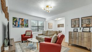 Una sala de estar con un sofá, sillones, una mesa de centro y un televisor. Hay cuadros enmarcados en la pared y un aparador con adornos.