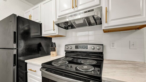 Una cocina con armarios blancos, un refrigerador negro y una estufa con cuatro hornillas.