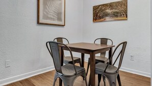 Un comedor con una mesa de madera y cuatro sillas, dos obras de arte enmarcadas en las paredes y una pared blanca con textura.