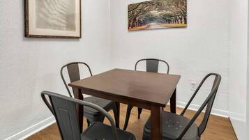 Un coin repas avec une table en bois et quatre chaises, des œuvres d’art encadrées accrochées aux murs et un mur blanc à la texture particulière.