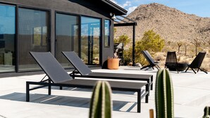 A modern outdoor patio with lounge chairs, a cactus, and a mountain backdrop. - Sacred Haven By Homestead Modern (Joshua Tree)