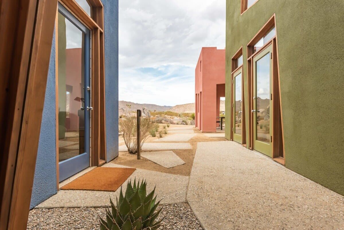 A modern building with large glass doors, a pathway, and a desert landscape in the background.