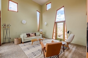 A spacious living room with a sofa, two chairs, a coffee table, a floor lamp, and a large window with a view. - Monument House by Homestead Modern (Joshua Tree)