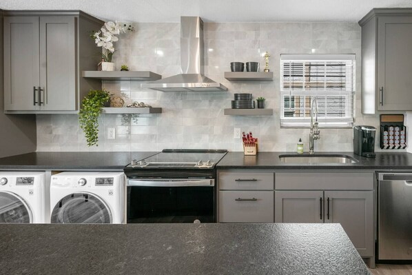 Une cuisine moderne dotée d’appareils électroménagers en acier inoxydable, de meubles de rangement gris et d’une fenêtre équipée de stores.