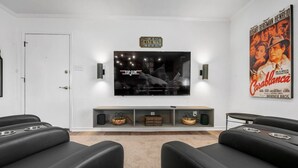 A modern living room with a flat-screen TV mounted on the wall, a popcorn machine, and a movie poster. - Cinema: 2 Bedroom, Walk to A&M, Comfy King Beds (Bryan)