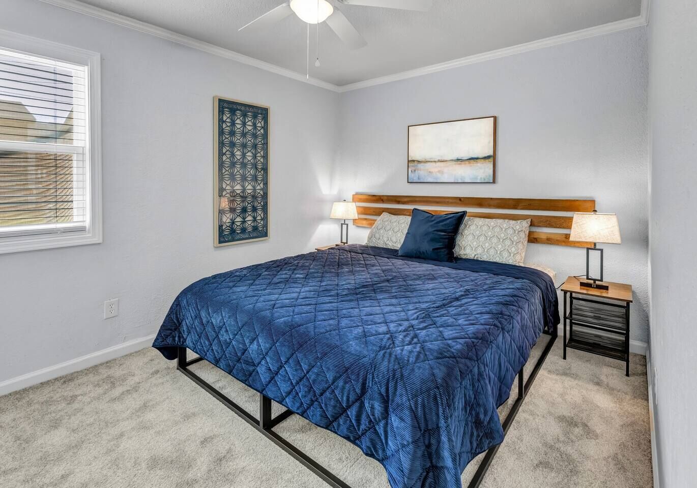 A bedroom with a bed, two bedside tables, a ceiling fan, and artwork on the walls.