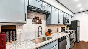 A modern kitchen with grey cabinets, a stainless steel refrigerator, a microwave, and a dishwasher. - Denali: 2 Bedroom, Walk to A&M, Comfy King Beds (Bryan)