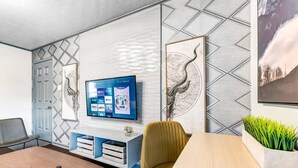 A modern living room with a flat-screen TV mounted on the wall, a wooden coffee table, a yellow armchair, and a small side table with a plant. - Denali: 2 Bedroom, Walk to A&M, Comfy King Beds (Bryan)