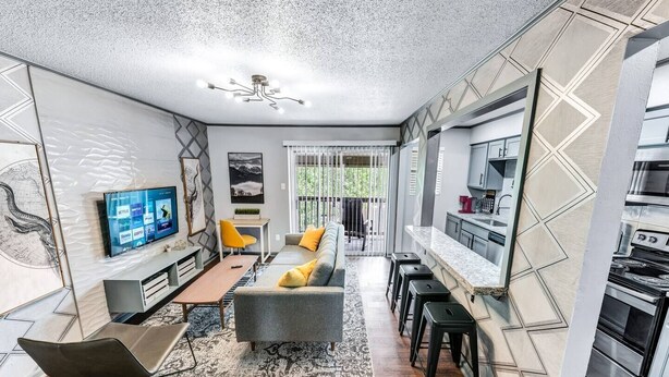 A modern kitchen with a built-in oven and a dining area with a gray sofa and yellow cushions. - Denali: 2 Bedroom, Walk to A&M, Comfy King Beds (Bryan)