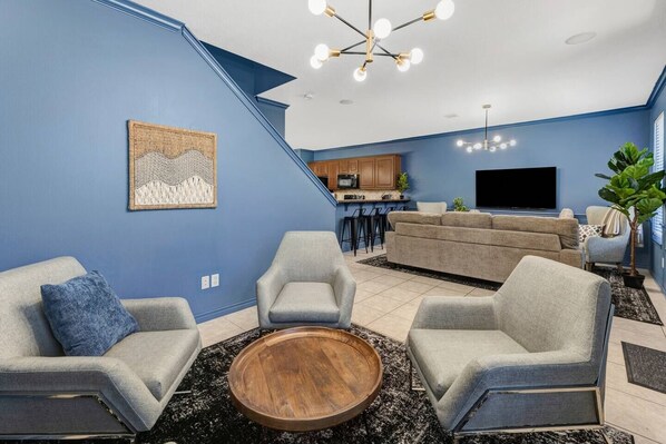 A modern living room with a staircase, grey sofas, a wooden coffee table, and a kitchen area with bar stools. - Comfy King Beds, Close to A&M (College Station)
