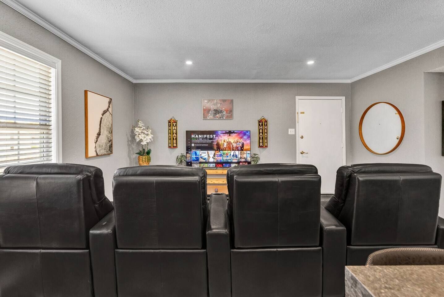 Une salle de cinéma maison équipée de quatre fauteuils en cuir noir, d’un tél éviseur à écran plat et d’un appareil à pop-corn.