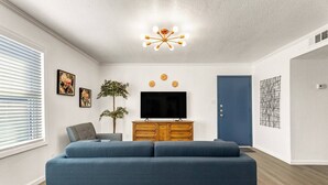 A modern living room with a blue sofa, wooden TV stand, and a ceiling light fixture. - Elise: 2 Bdrm,  Walk to A&M, Comfy King Beds (Bryan)