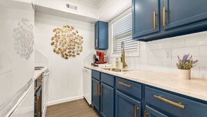 A modern kitchen with blue cabinets, a white countertop, and a decorative leaf wall art. - Elise: 2 Bdrm,  Walk to A&M, Comfy King Beds (Bryan)