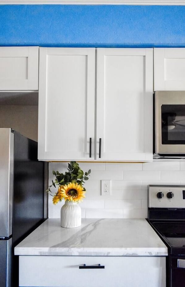 A kitchen with white cabinets, a marble countertop, a stainless steel refrigerator, an oven, and a microwave.