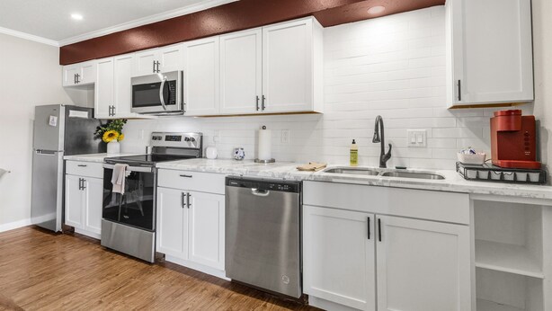 A modern kitchen with white cabinets, stainless steel appliances, and a wooden floor. - The Zone: Blocks from Texas A&M, Comfy King Bed (Bryan)