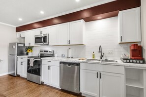 Cozinha moderna com armários brancos, eletrodomésticos de aço inoxidável e piso de madeira.
