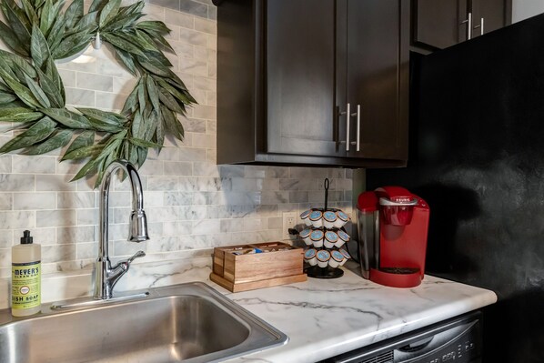 A kitchen with a stainless steel sink, a coffee maker, a dish soap bottle, and a wooden box.