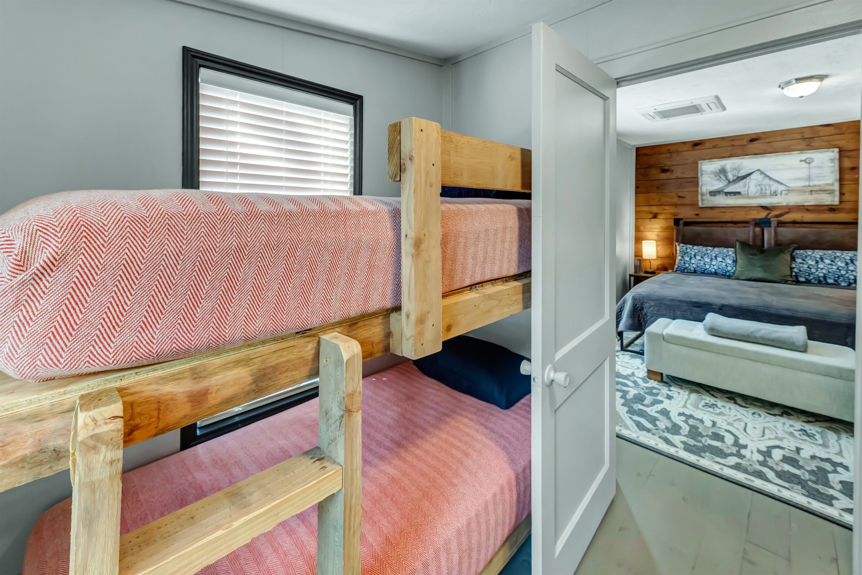 Een slaapkamer met een stapelbed, een sprei met een herringbone patroon, een houten hoofdbord en een nachtkastje met een lamp.