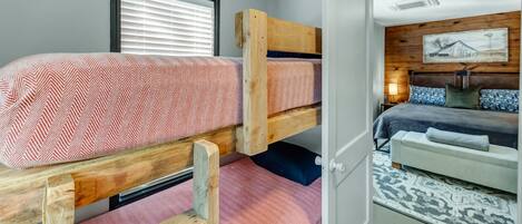 Een slaapkamer met een stapelbed, een sprei met een herringbone patroon, een houten hoofdbord en een nachtkastje met een lamp.