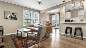 Ein modernes Wohnzimmer mit Sofa, Couchtisch und Teppich. Es gibt eine Küchenzeile mit Arbeitsplatte und Barhocker.