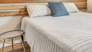Ein Schlafzimmer mit hölzernem Kopfende, gemusterten Betttextilien und einem kleinen runden Tisch.