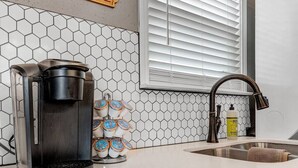 Eine Küche mit Kaffeemaschine, einer Aufbewahrungsboxen-Leiste, einem Spülbecken und einem Fenster mit Jalousien.