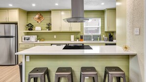 A modern kitchen with a central island, green cabinetry, stainless steel appliances, and a decorative wall piece.